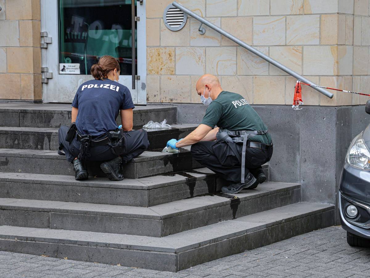 Eine Polizistin und ein Polizist hocken auf den Stufen der Synagoge und sichern Spuren.