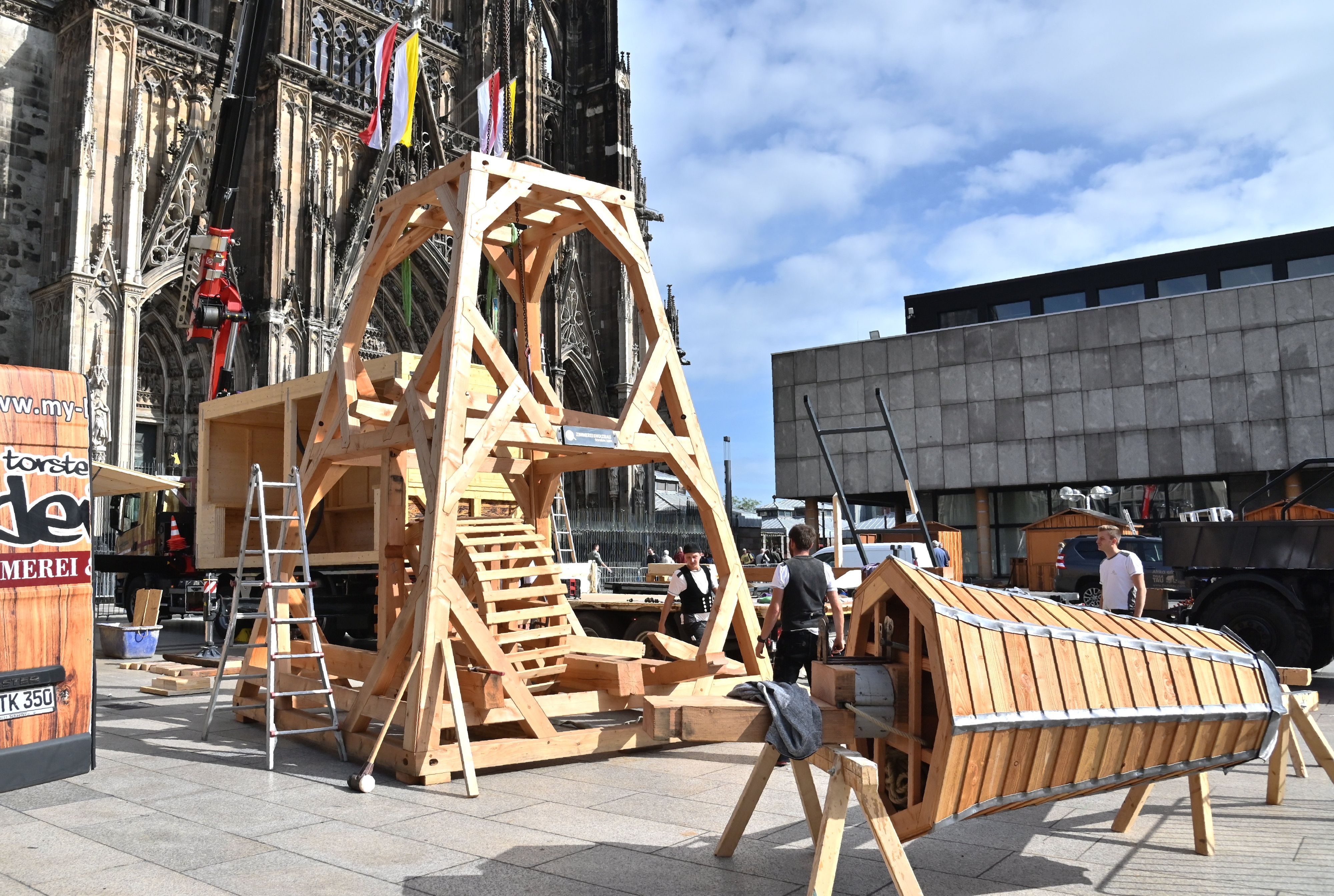 Ein Teil eines hölzernen Krans steht vor dem Kölner Dom, die Spitze liegt noch daneben.