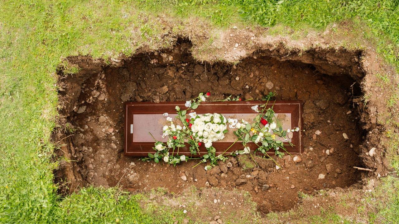 Ein Sarg mit Blumen in einem geöffneten Grab.