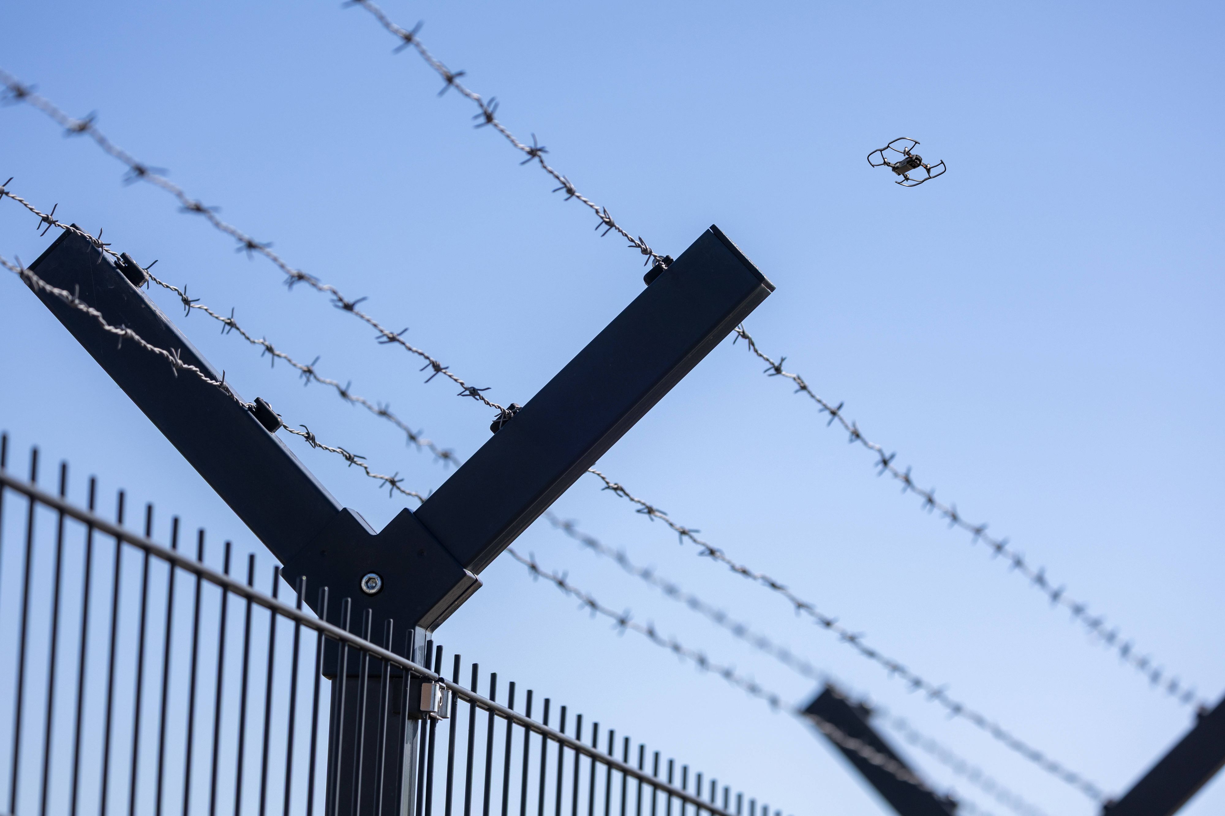 Fliegende Drohne am Horizont hinter einem Sicherheitszaun mit Stacheldraht.