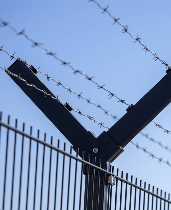 Fliegende Drohne am Horizont hinter einem Sicherheitszaun mit Stacheldraht.