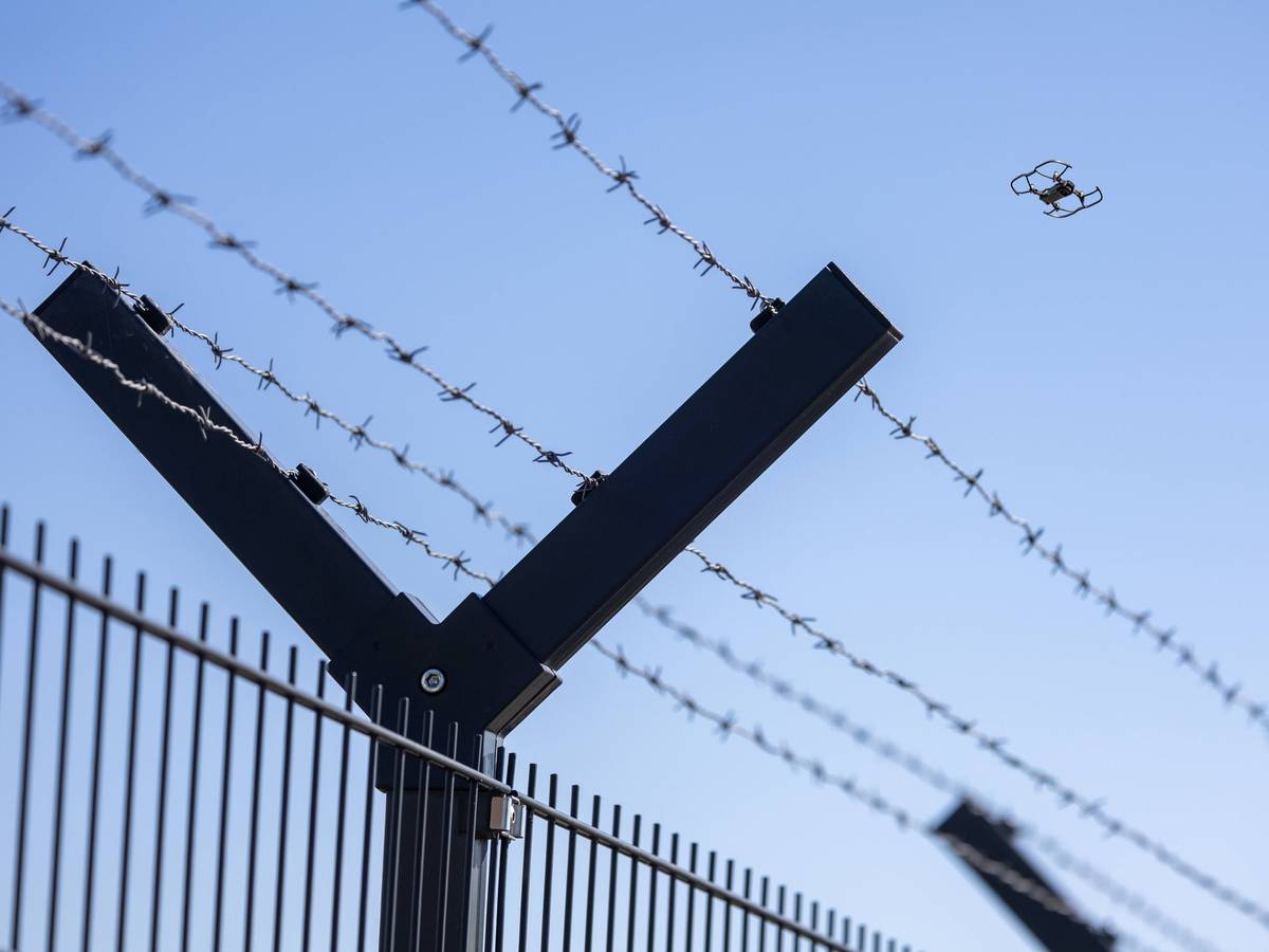Fliegende Drohne am Horizont hinter einem Sicherheitszaun mit Stacheldraht.