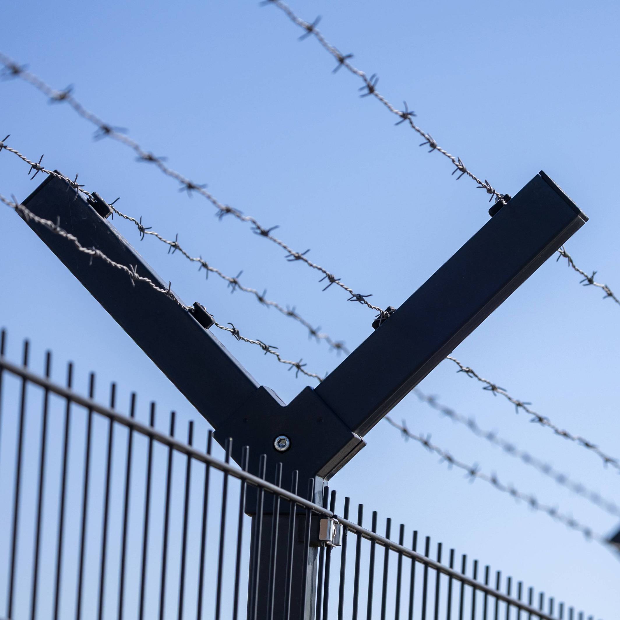 Fliegende Drohne am Horizont hinter einem Sicherheitszaun mit Stacheldraht.