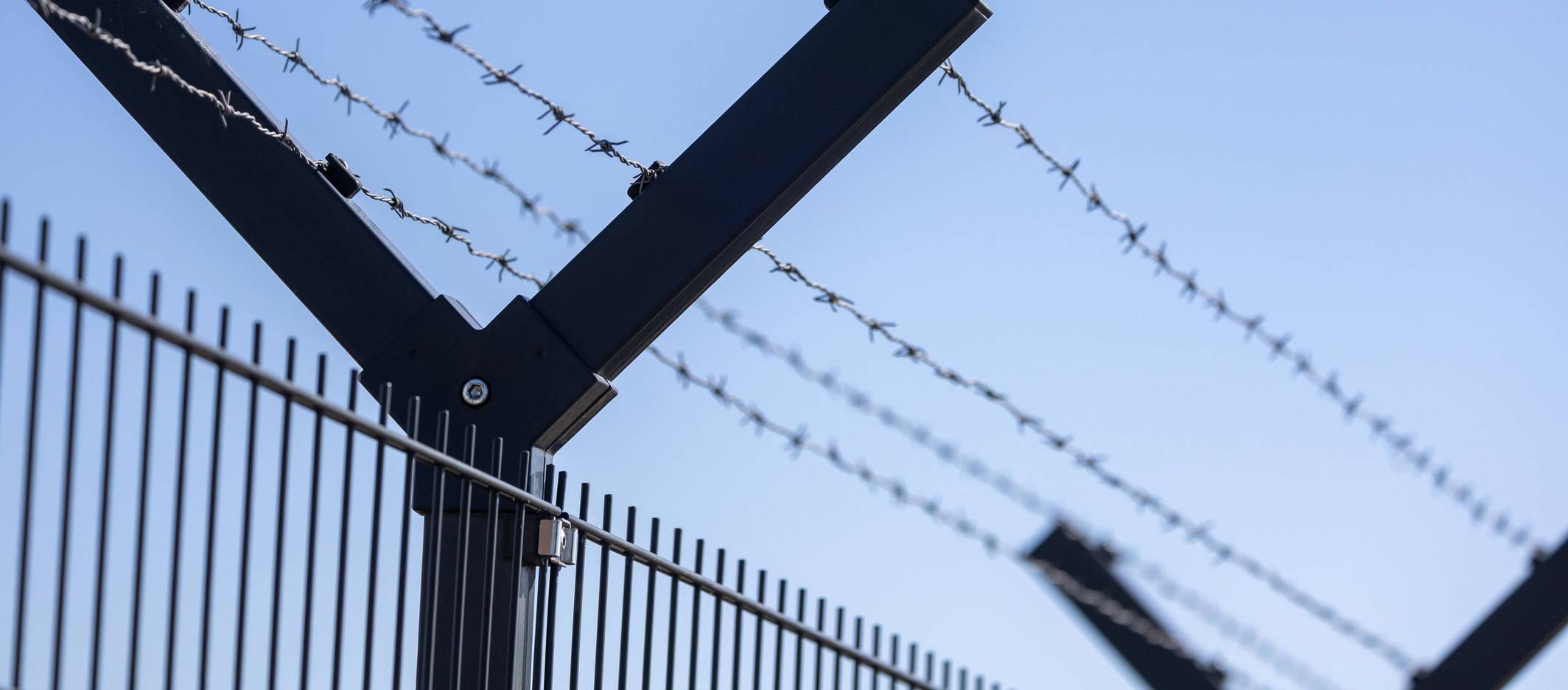 Fliegende Drohne am Horizont hinter einem Sicherheitszaun mit Stacheldraht.