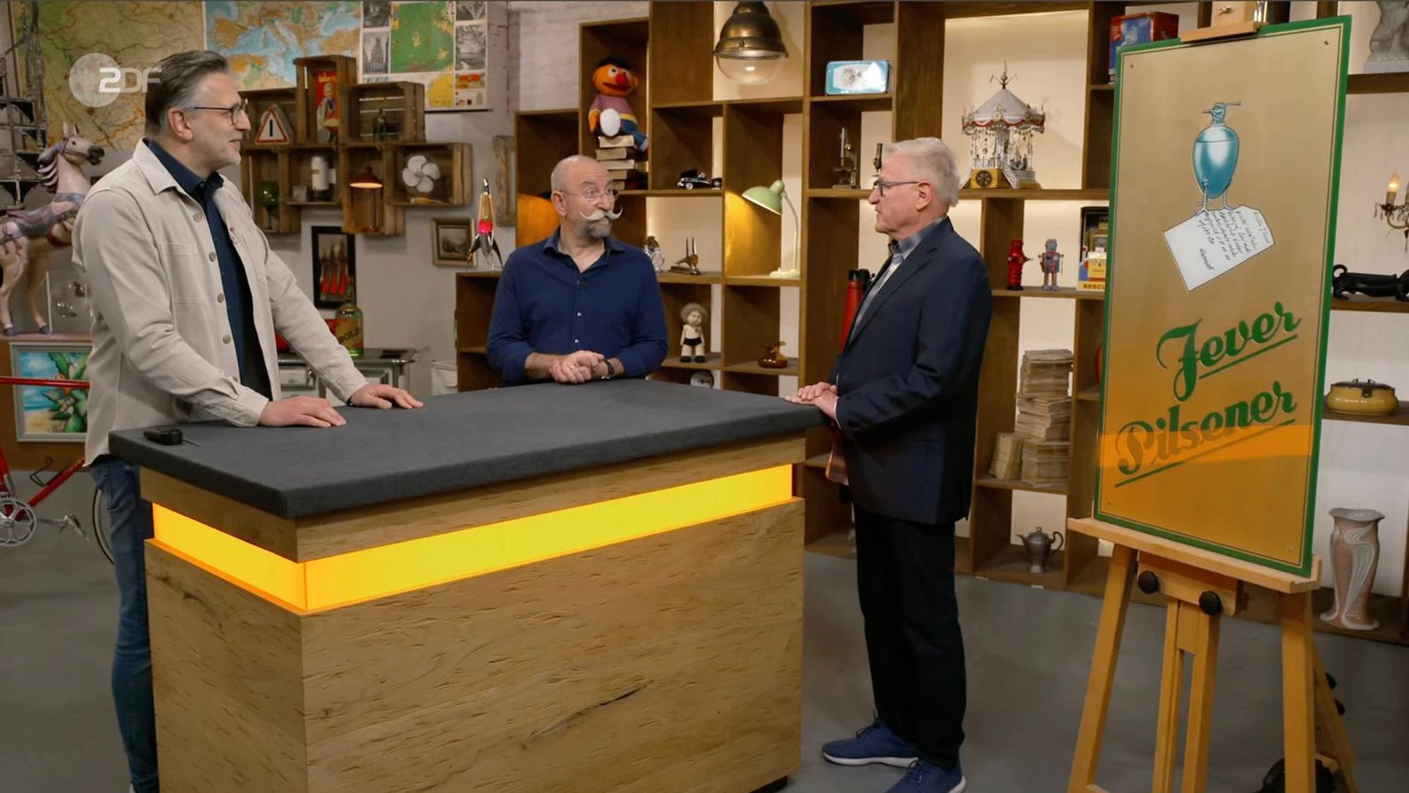 Mehr als 35 Jahre hing das alte Jever-Schild an Willis Wand. Weil er mittlerweile die Biermarke gewechselt hatte, wollte er es in der Mittwochsausgabe von „Bares für Rares“ (ZDF) loswerden. Doch Experte Detlev Kümmel erkannte schnell, dass es sich um eine echte Rarität handelte und sorgte damit für eine überraschende Expertise. (Bild: ZDF)