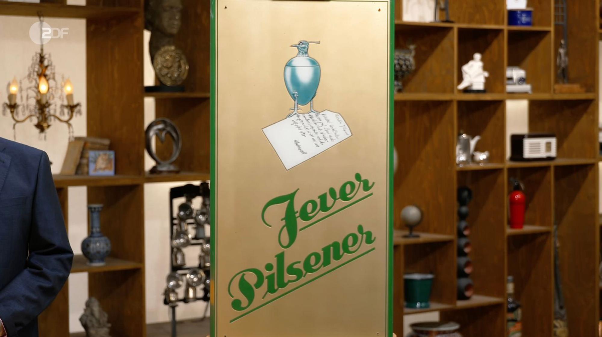 Das Werbeschild war von Jever Pilsener, das seit 1848 in der friesischen Stadt Jever gebraut wurde. Lichter fiel jedoch vor allem das ungewöhnliche Motiv ins Auge: Zu sehen war ein Kiebitz-Becher, der einst als Markenzeichen der Brauerei diente und eng mit der Geschichte der Stadt Jever verbunden war. (Bild: ZDF)