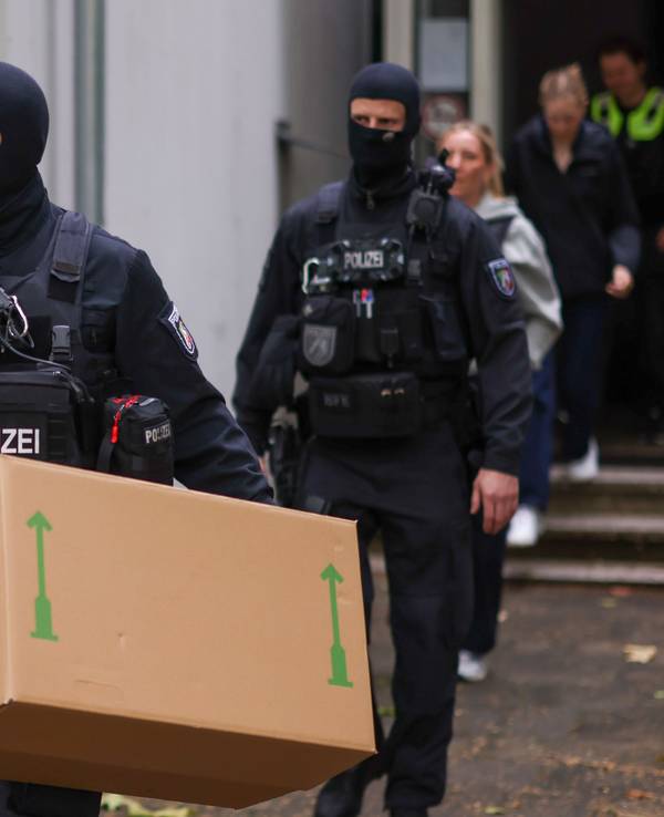 Zwei vermummte Polizisten verlassen ein Gebäude, einer trägt einen großen Karton.