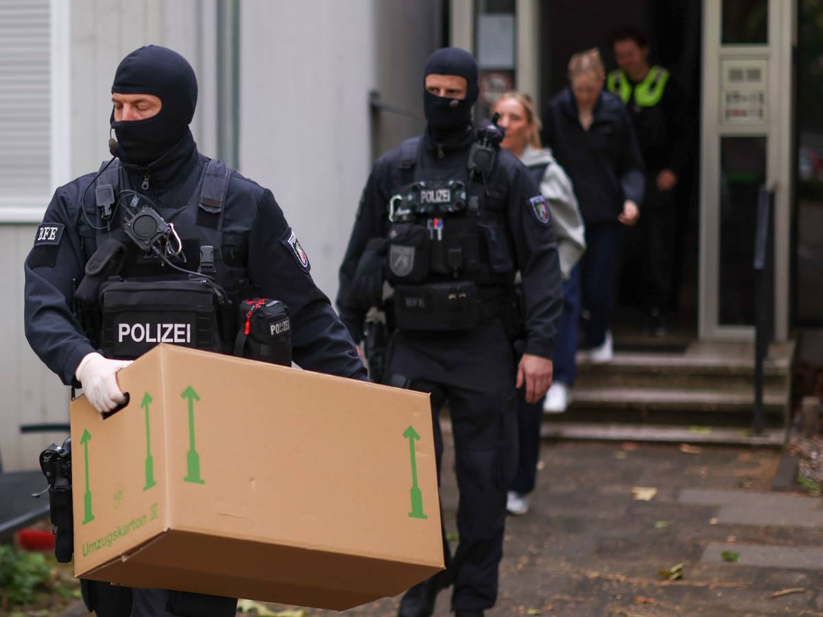 Zwei vermummte Polizisten verlassen ein Gebäude, einer trägt einen großen Karton.
