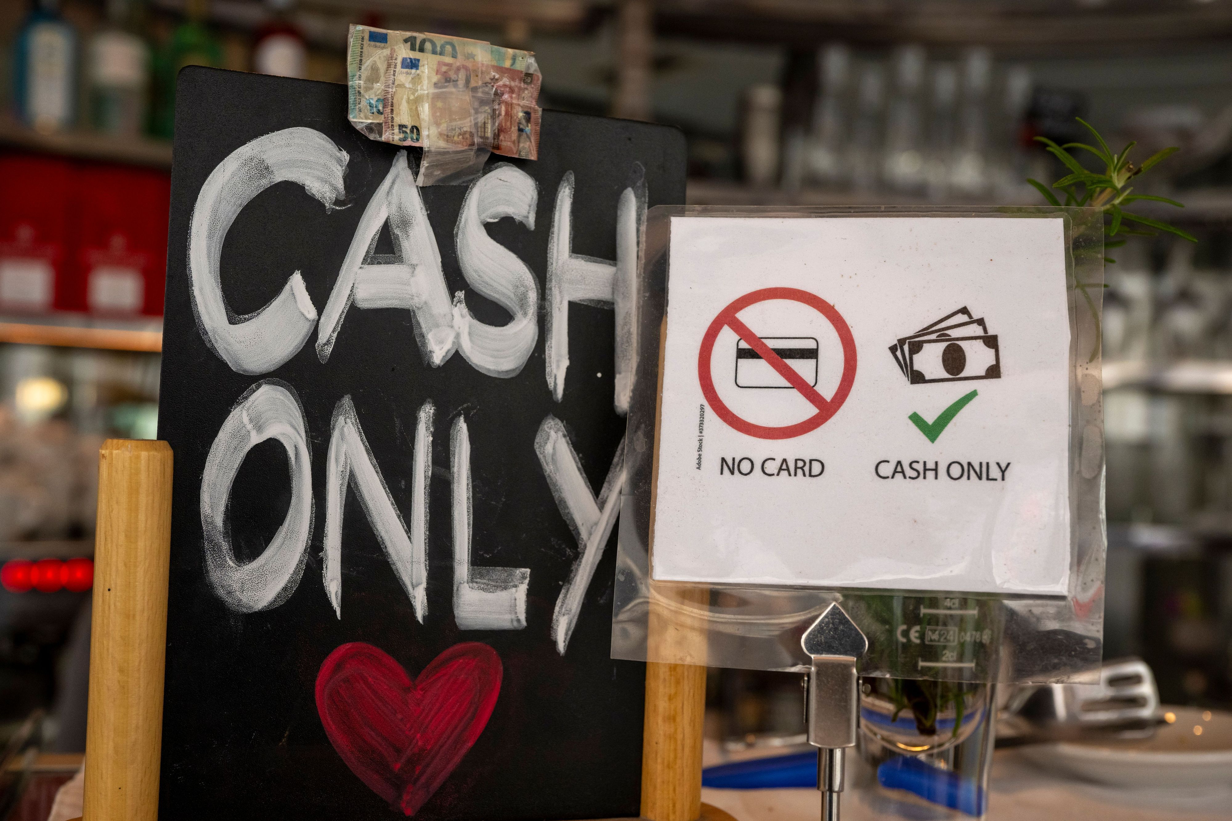 Ein Schild mit der Aufschrift „No Card – Cash Only“ steht in einem Café.
