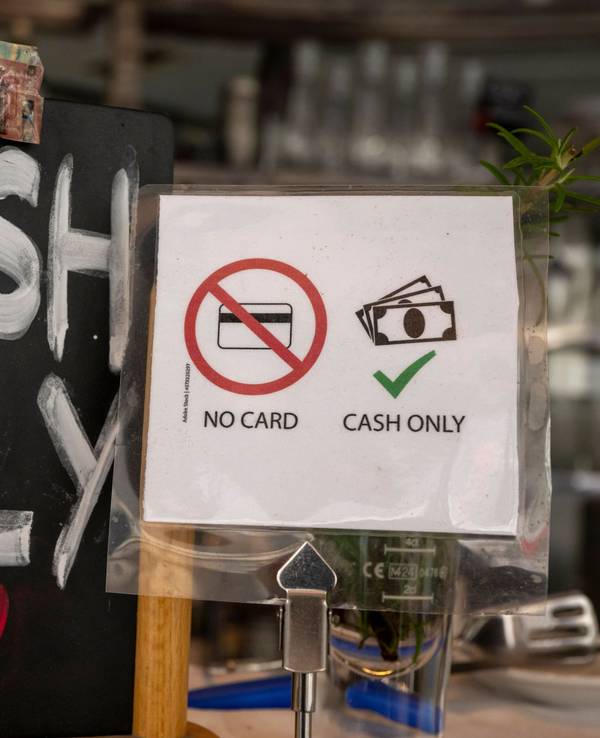 Ein Schild mit der Aufschrift „No Card – Cash Only“ steht in einem Café.