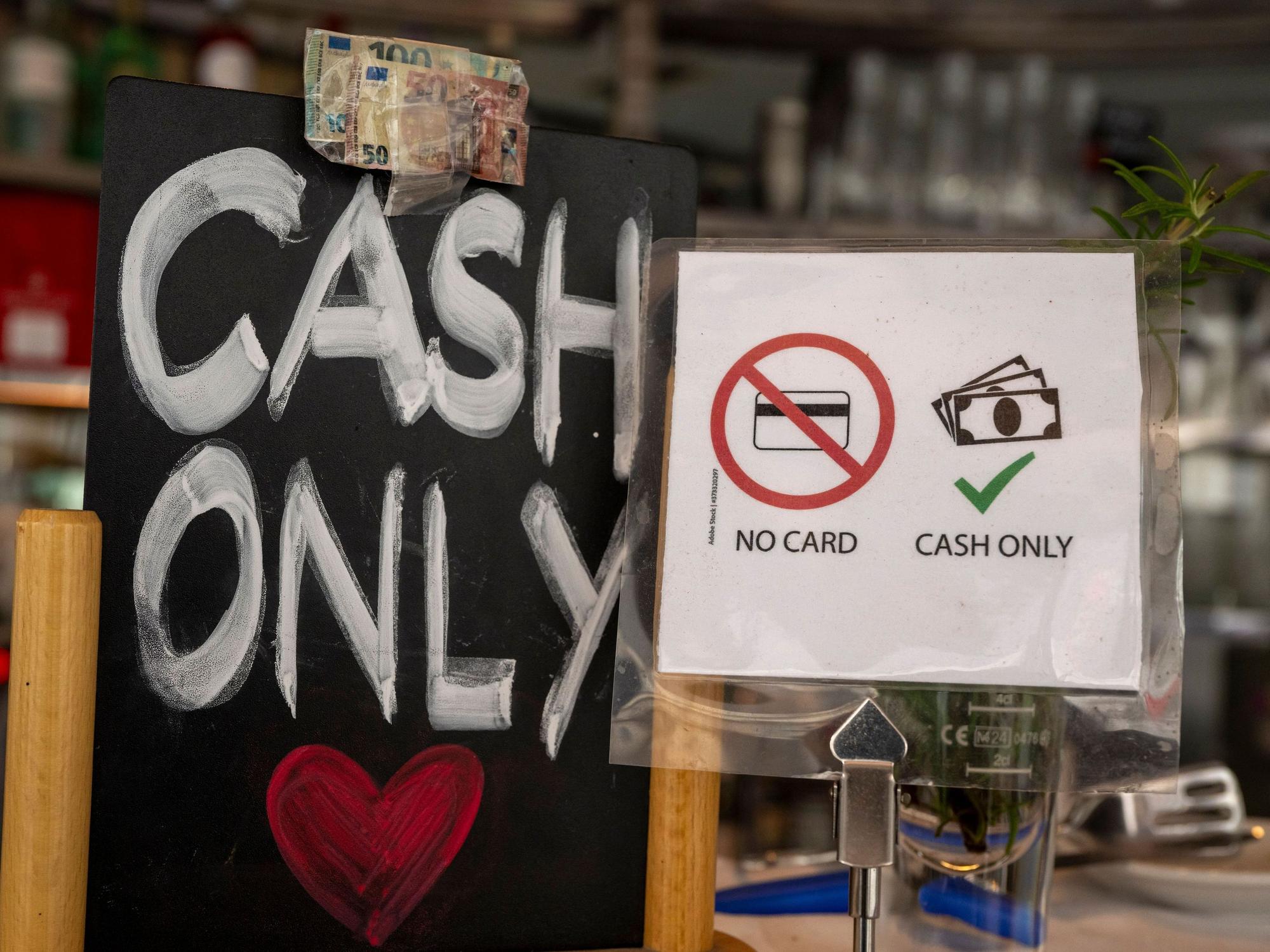 Ein Schild mit der Aufschrift „No Card – Cash Only“ steht in einem Café.