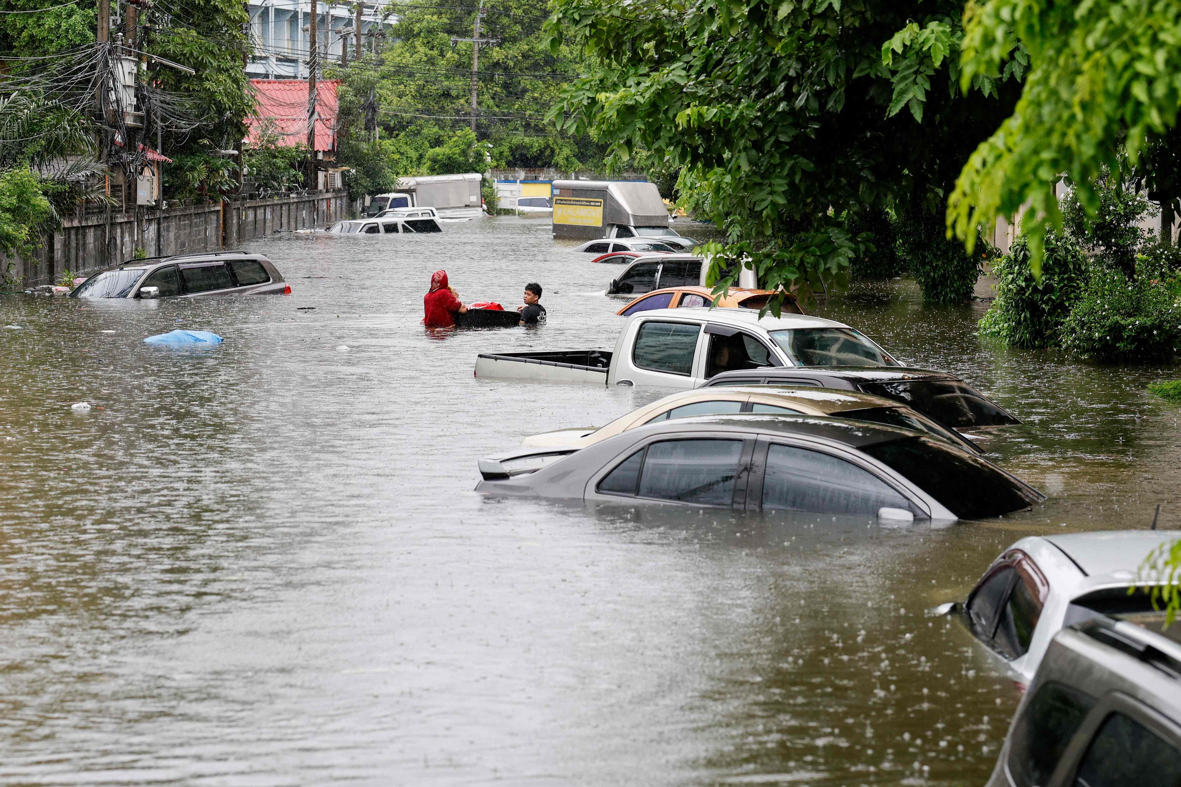 Menschen gehen am 26. September 2026 in Bangkok neben Autos entlang, die nach heftigen Regenfällen überflutet wurden. Die Behörden von Bangkok riefen für die gesamte thailändische Hauptstadt den Hochwasser-Notstand aus.