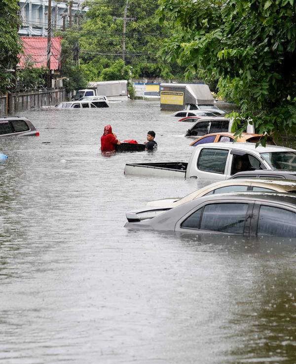 Menschen gehen am 26. September 2026 in Bangkok neben Autos entlang, die nach heftigen Regenfällen überflutet wurden. Die Behörden von Bangkok riefen für die gesamte thailändische Hauptstadt den Hochwasser-Notstand aus.
