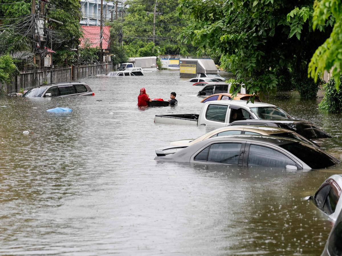 Menschen gehen am 26. September 2026 in Bangkok neben Autos entlang, die nach heftigen Regenfällen überflutet wurden. Die Behörden von Bangkok riefen für die gesamte thailändische Hauptstadt den Hochwasser-Notstand aus.