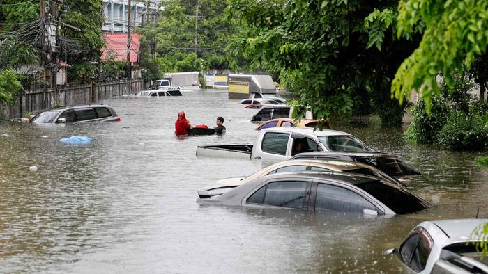 Menschen gehen am 26. September 2026 in Bangkok neben Autos entlang, die nach heftigen Regenfällen überflutet wurden. Die Behörden von Bangkok riefen für die gesamte thailändische Hauptstadt den Hochwasser-Notstand aus.