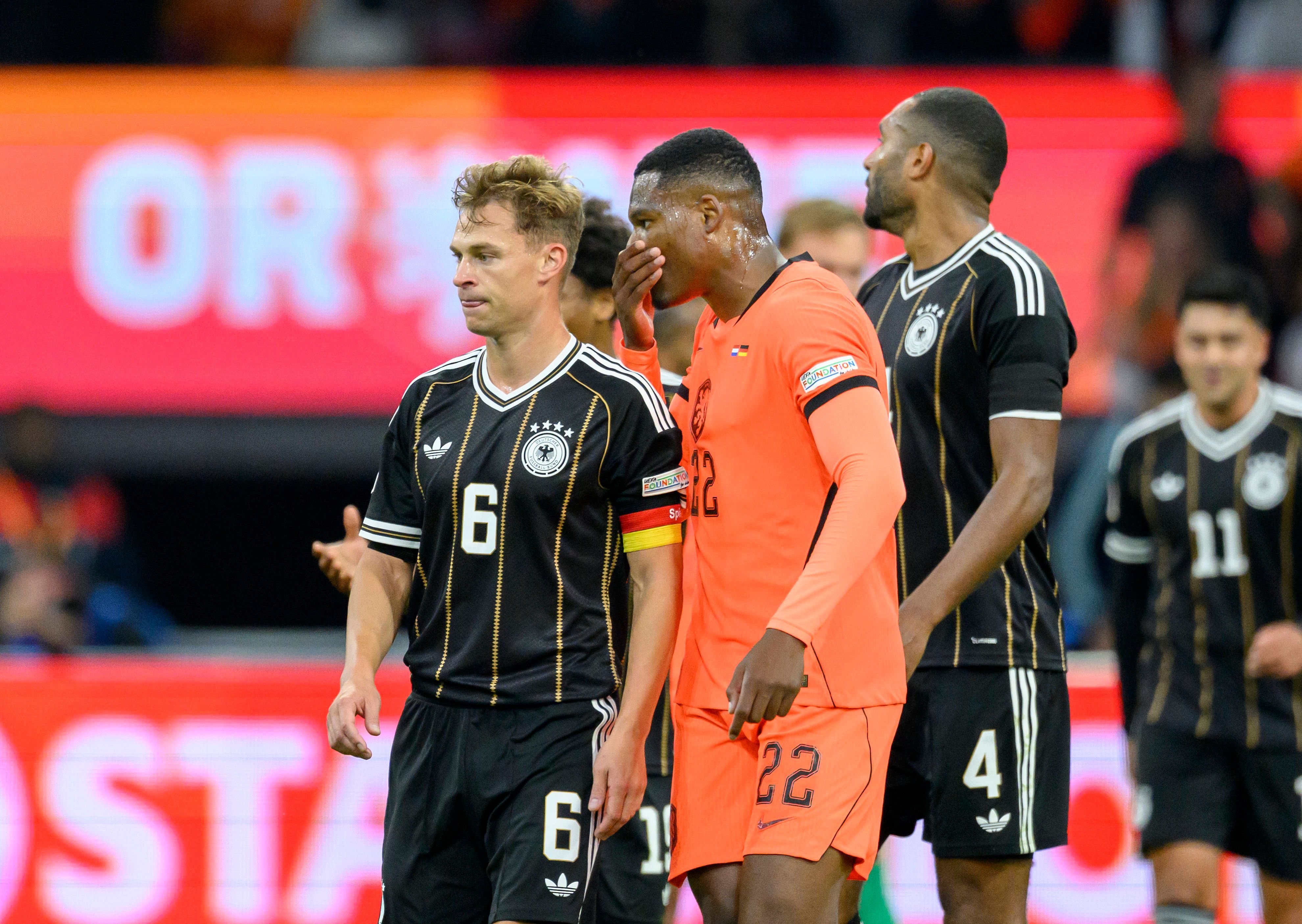 Denzel Dumfries sagt etwas zu Joshua Kimmich und hält dabei die Hand vors Gesicht.