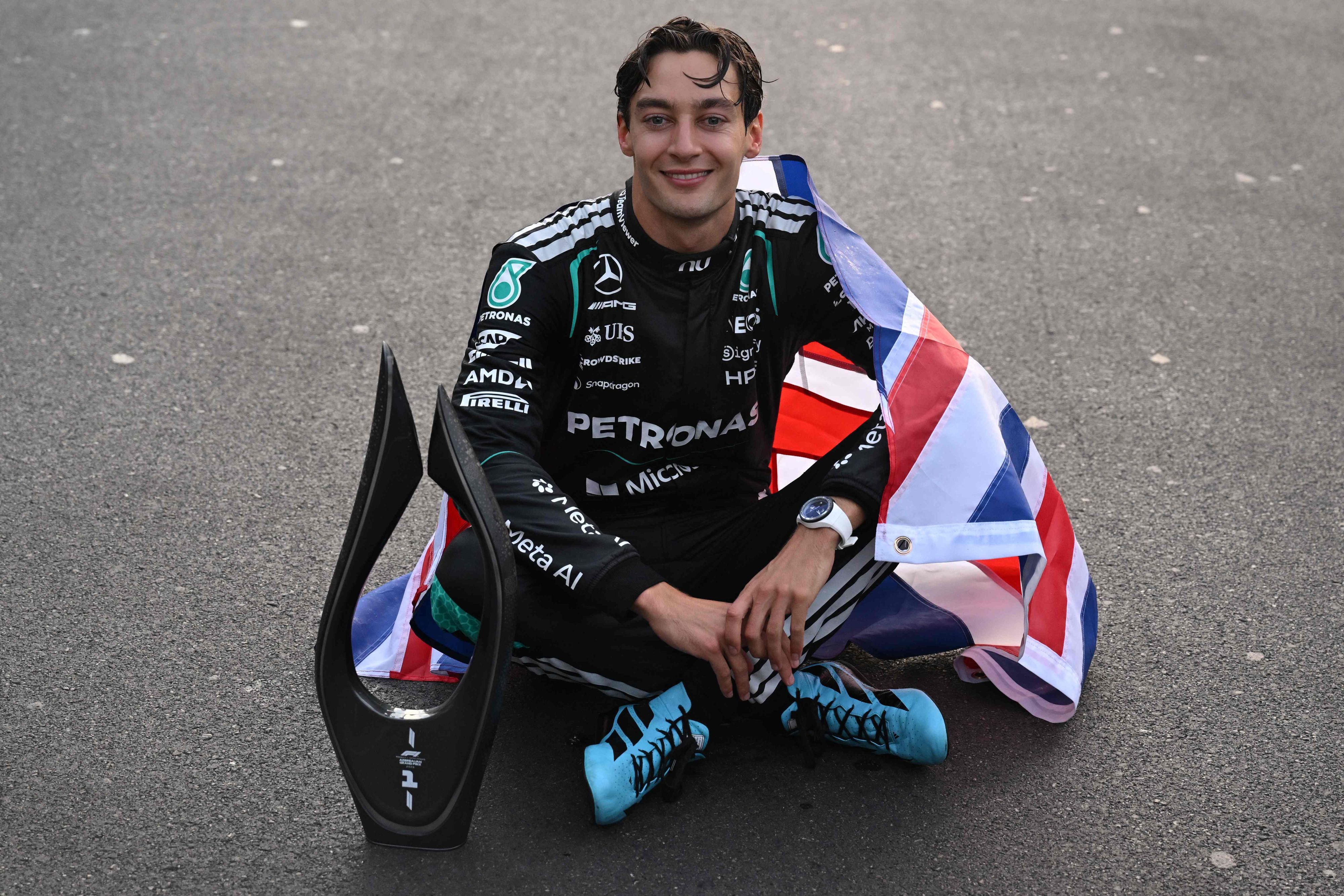 George Russell sitzt mit Pokal auf dem Asphalt.
