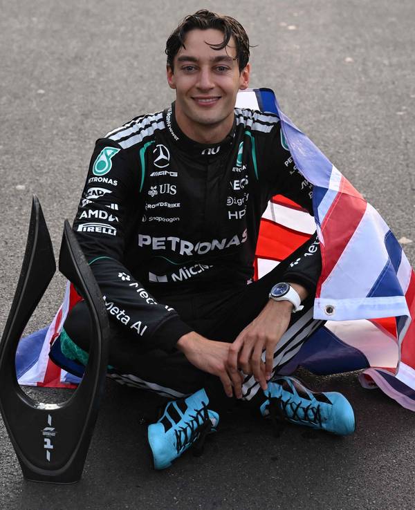 George Russell sitzt mit Pokal auf dem Asphalt.
