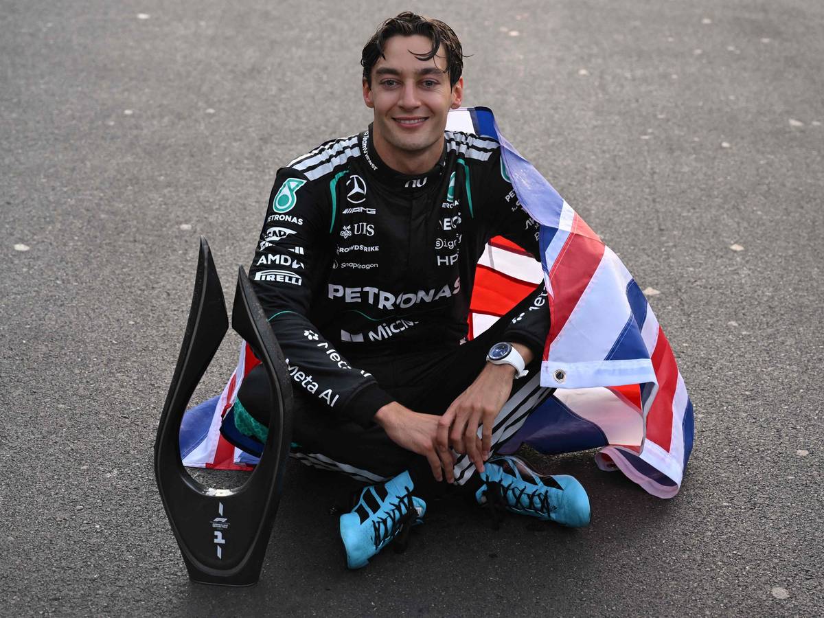 George Russell sitzt mit Pokal auf dem Asphalt.