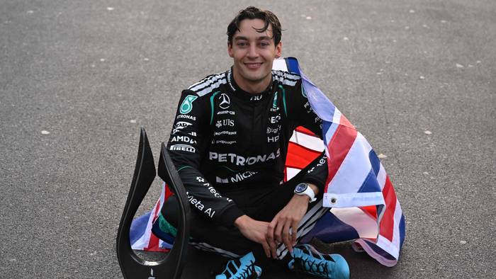 George Russell sitzt mit Pokal auf dem Asphalt.