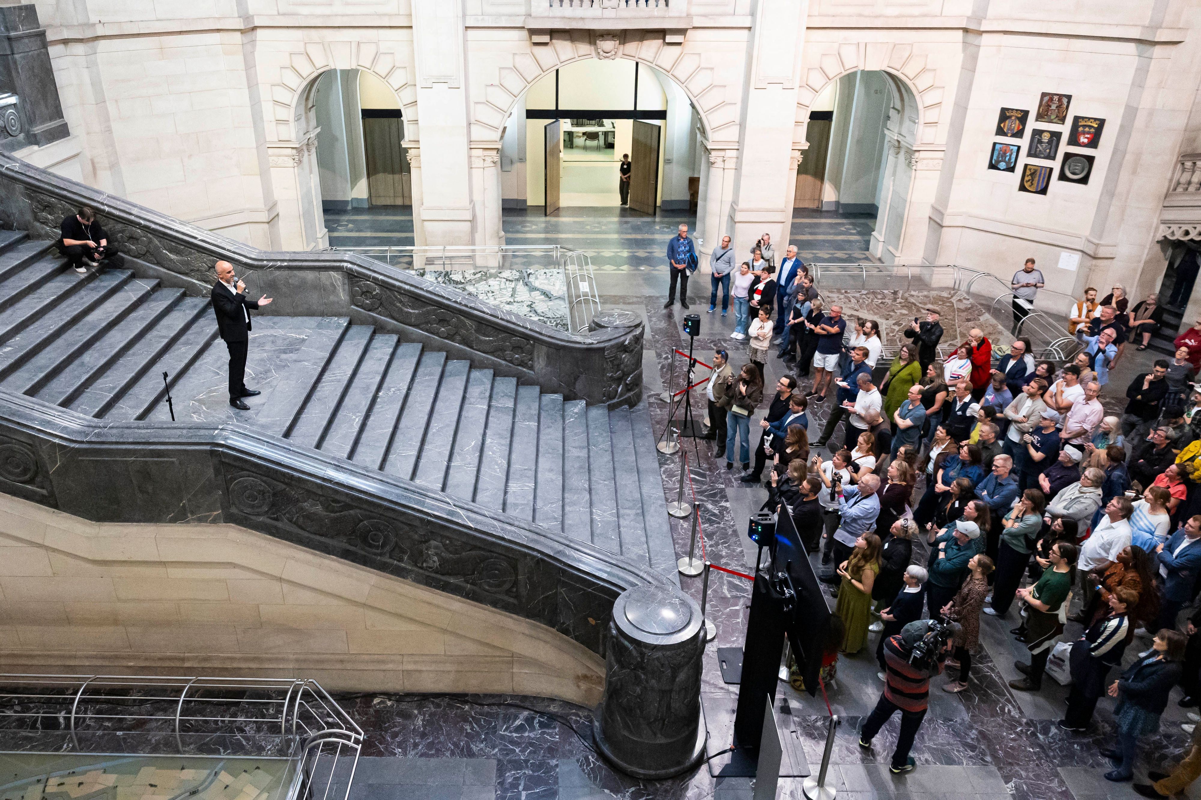 Belit Onay steht auf einer breiten Treppe und spricht zur zahlreichen Presseleuten, die sich am Fuß der Treppe knubbeln.