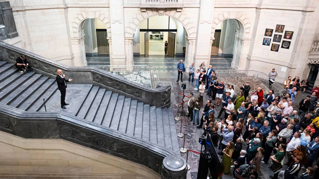 Belit Onay steht auf einer breiten Treppe und spricht zur zahlreichen Presseleuten, die sich am Fuß der Treppe knubbeln.