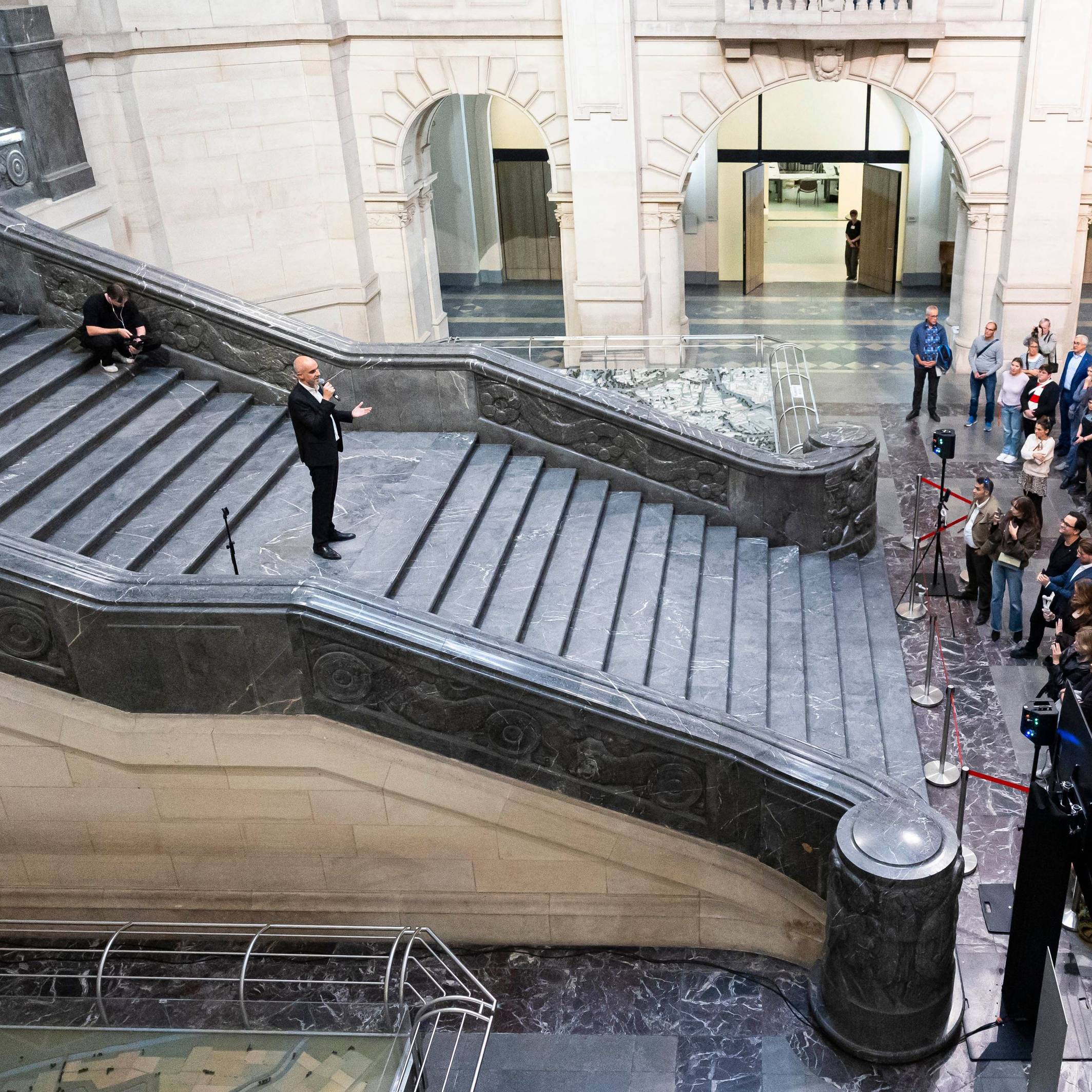 Belit Onay steht auf einer breiten Treppe und spricht zur zahlreichen Presseleuten, die sich am Fuß der Treppe knubbeln.