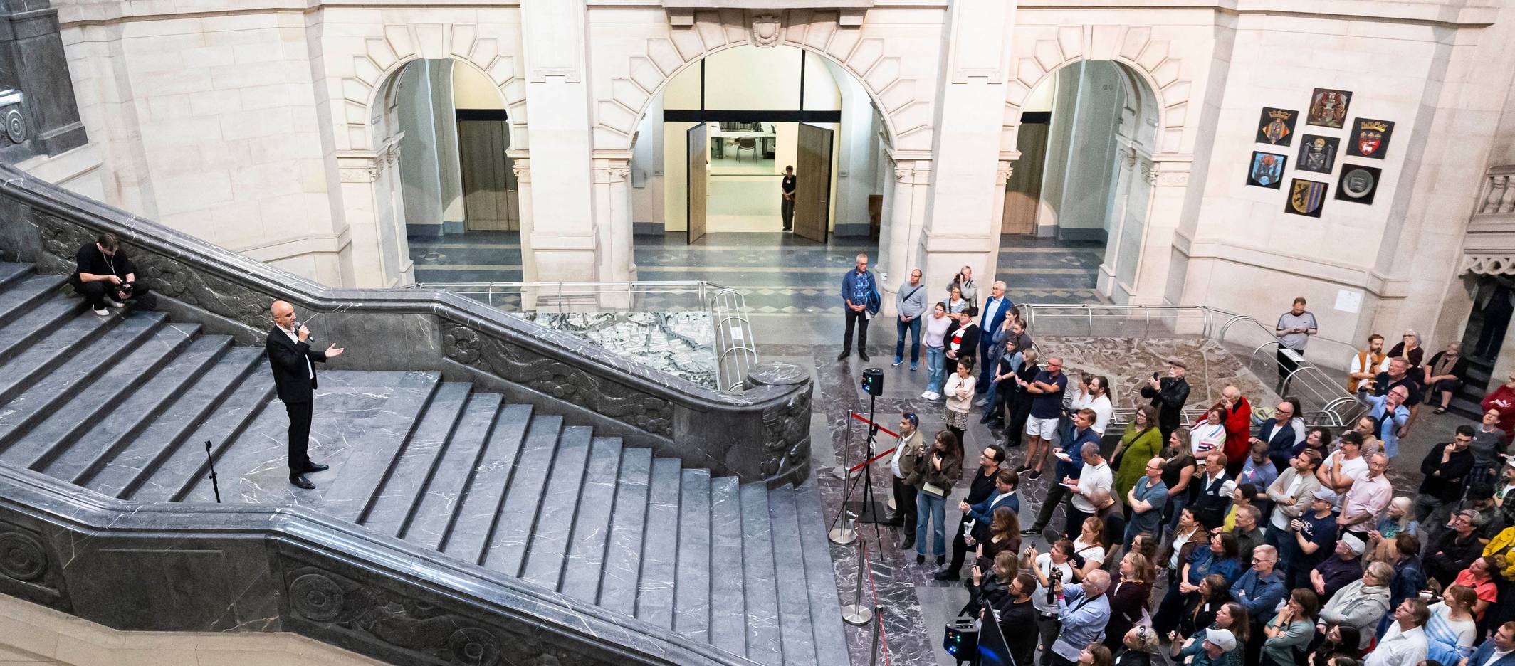 Belit Onay steht auf einer breiten Treppe und spricht zur zahlreichen Presseleuten, die sich am Fuß der Treppe knubbeln.