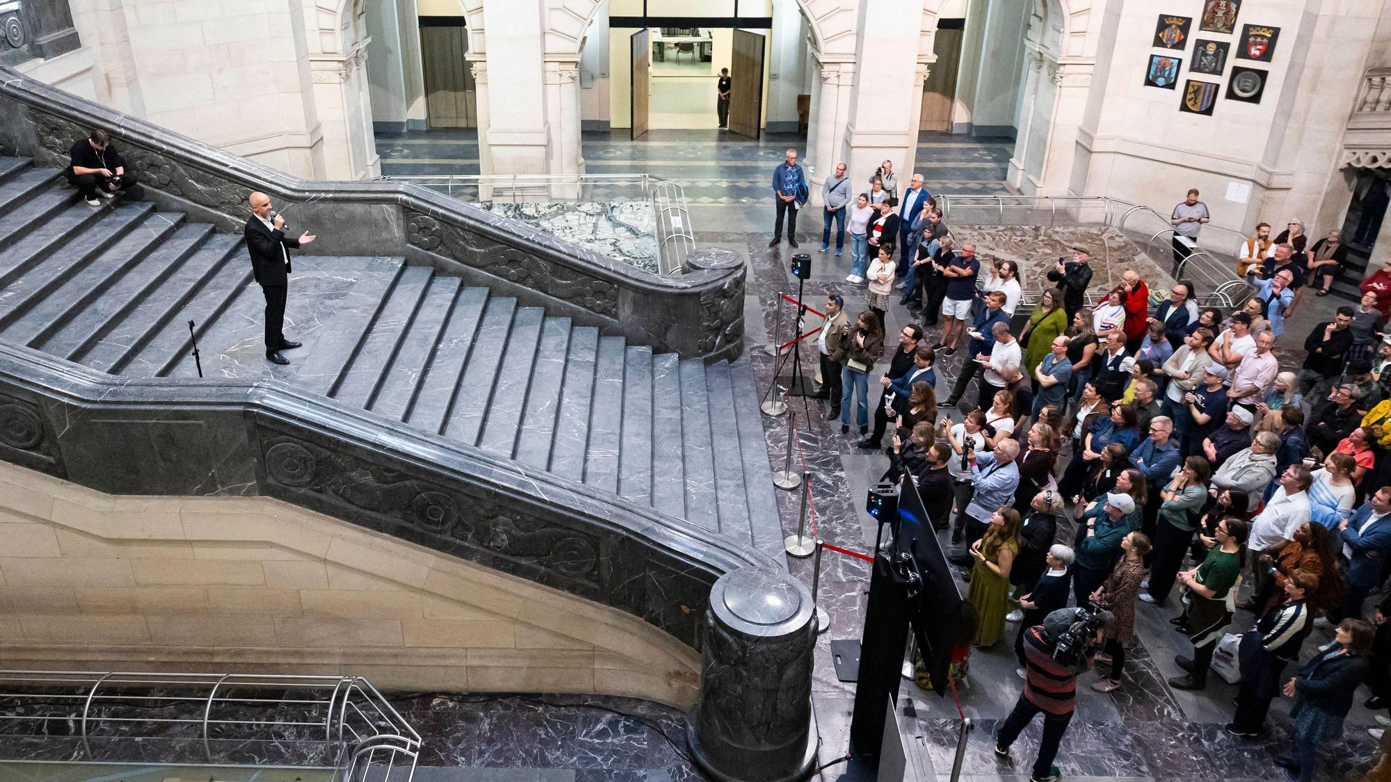 Belit Onay steht auf einer breiten Treppe und spricht zur zahlreichen Presseleuten, die sich am Fuß der Treppe knubbeln.