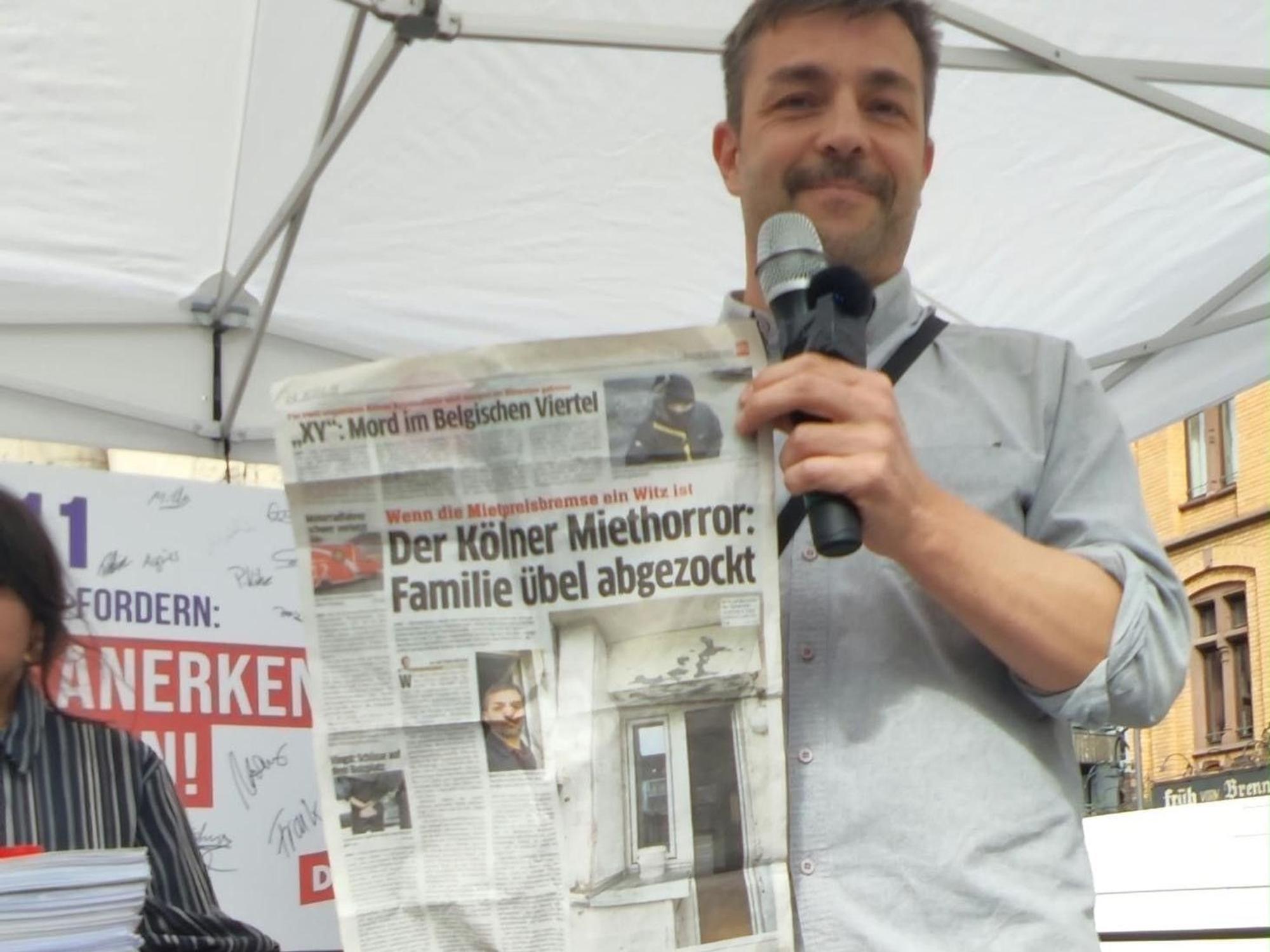 Ein Mann hält einen EXPRESS-Artikel hoch mit der Überschrift „Der Kölner Miethorror: Familie übel abgezockt.“