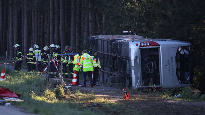 Kräfte von Feuerwehr und Polizei sind an einem Bus im Einsatz, der auf der Seite liegt.