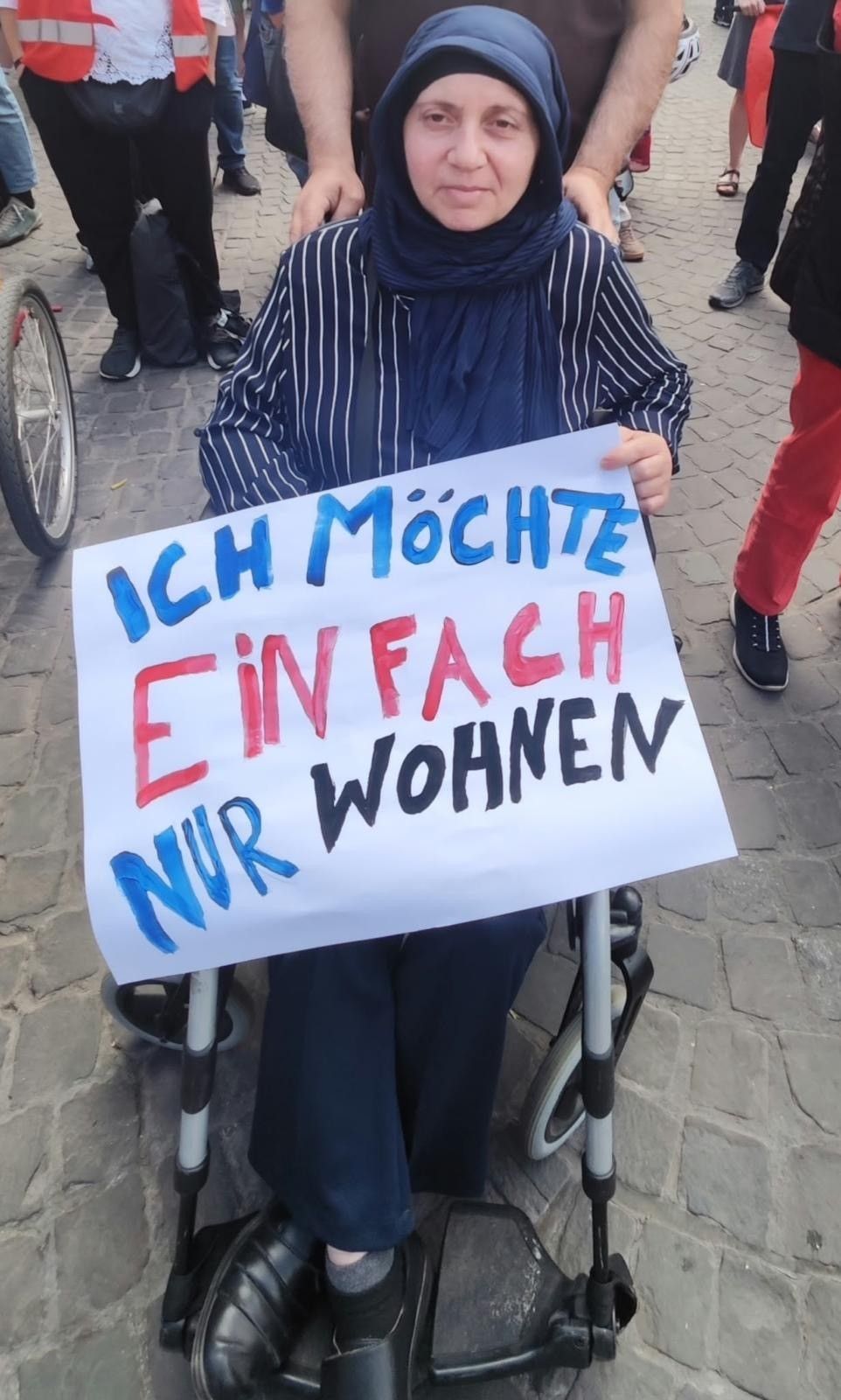 Die Frau, die im Rollstuhl sitzt, hält ein Plakat fest mit der Aufschrift „Ich möchte einfach nur wohnen“.