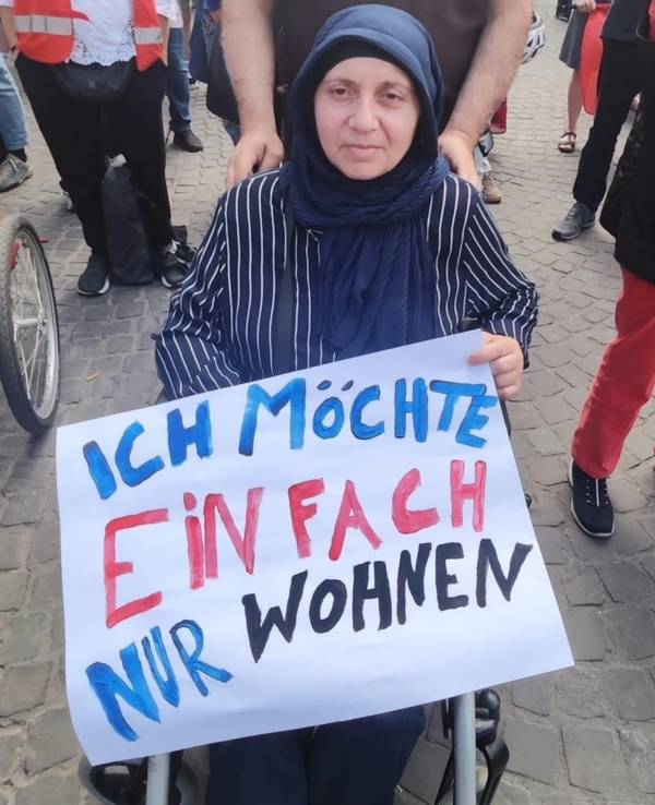 Die Frau, die im Rollstuhl sitzt, hält ein Plakat fest mit der Aufschrift „Ich möchte einfach nur wohnen“.