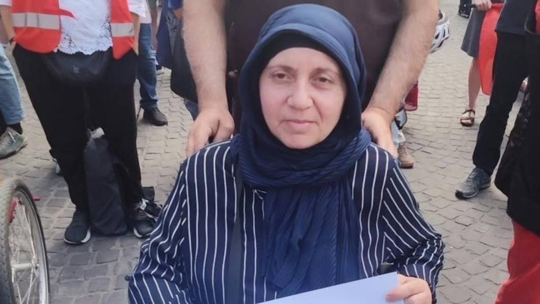 Die Frau, die im Rollstuhl sitzt, hält ein Plakat fest mit der Aufschrift „Ich möchte einfach nur wohnen“.