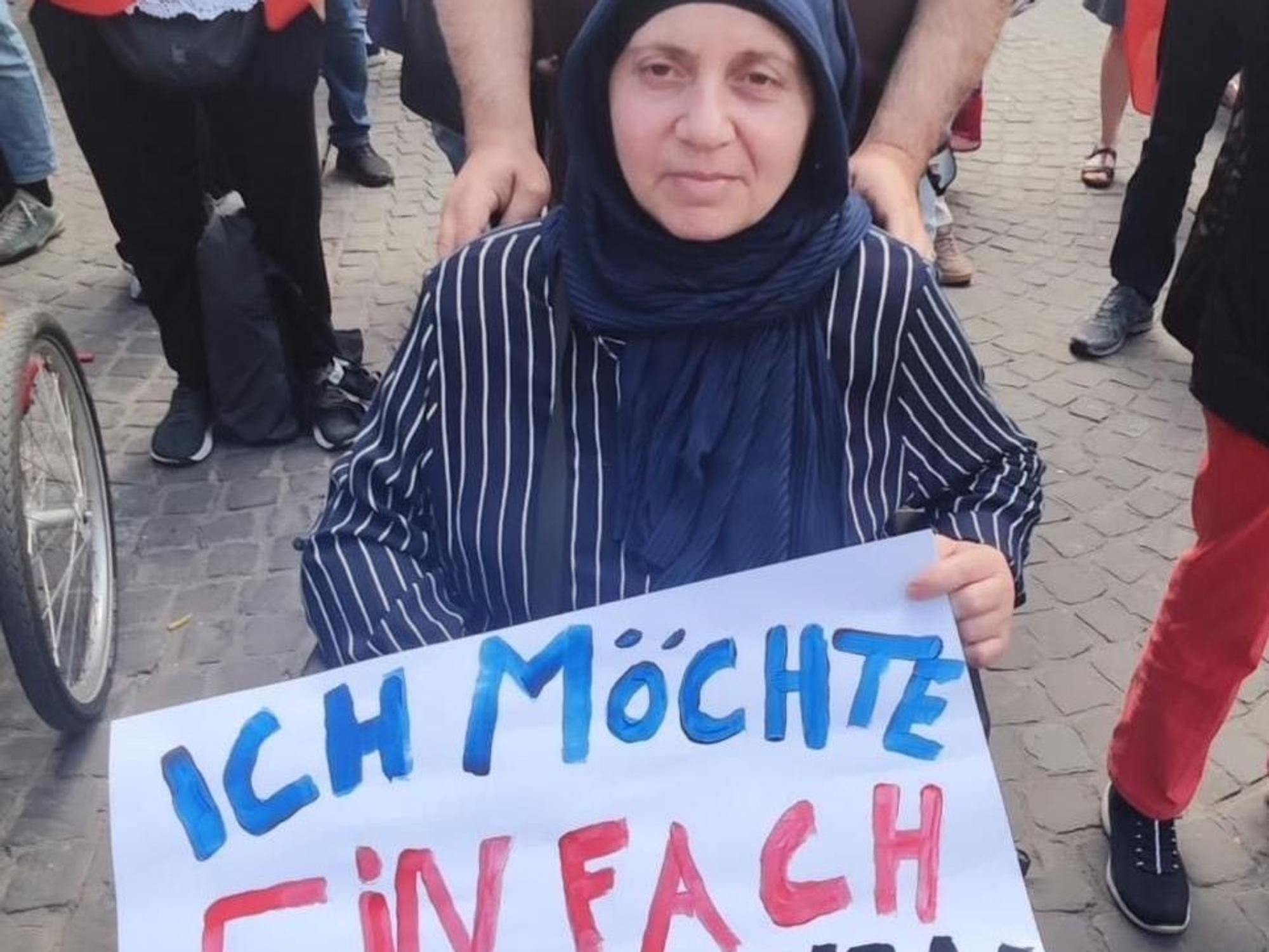 Die Frau, die im Rollstuhl sitzt, hält ein Plakat fest mit der Aufschrift „Ich möchte einfach nur wohnen“.