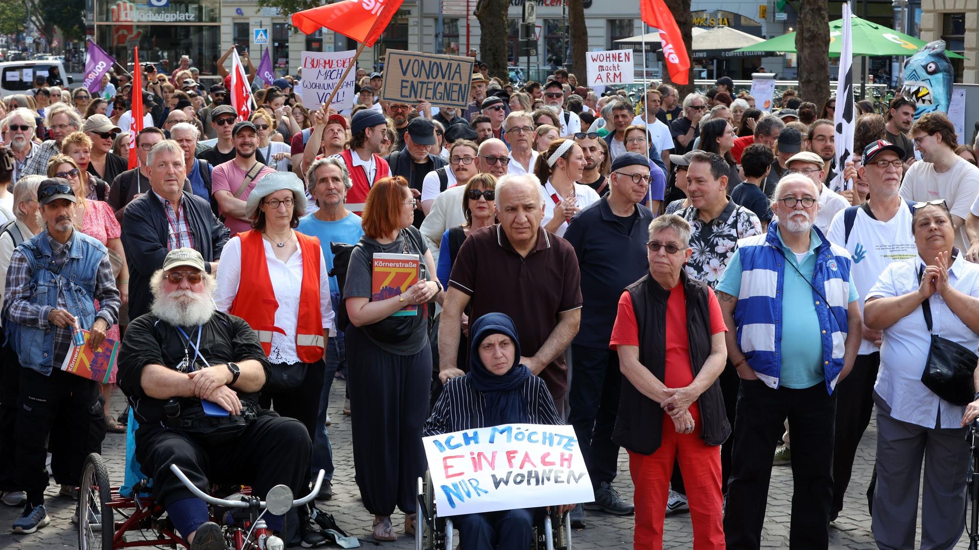 Zahlreiche Menschen nehmen an einer Kundgebung teil, eine Frau im Rollstuhl hält ein Plakat mit der Aufschrift „Ich möche einfach nur wohnen“.