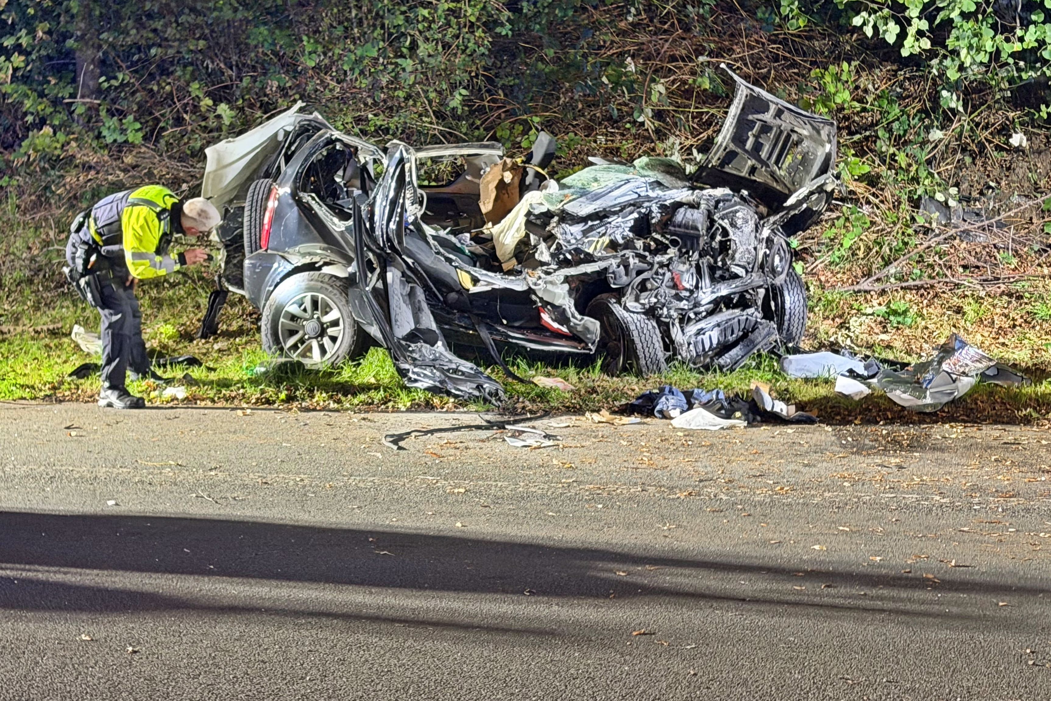 Ein Polizeibeamter untersucht ein zerstörtes Fahrzeug nach einem tödlichen Unfall an einer Autobahnausfahrt in Wuppertal.