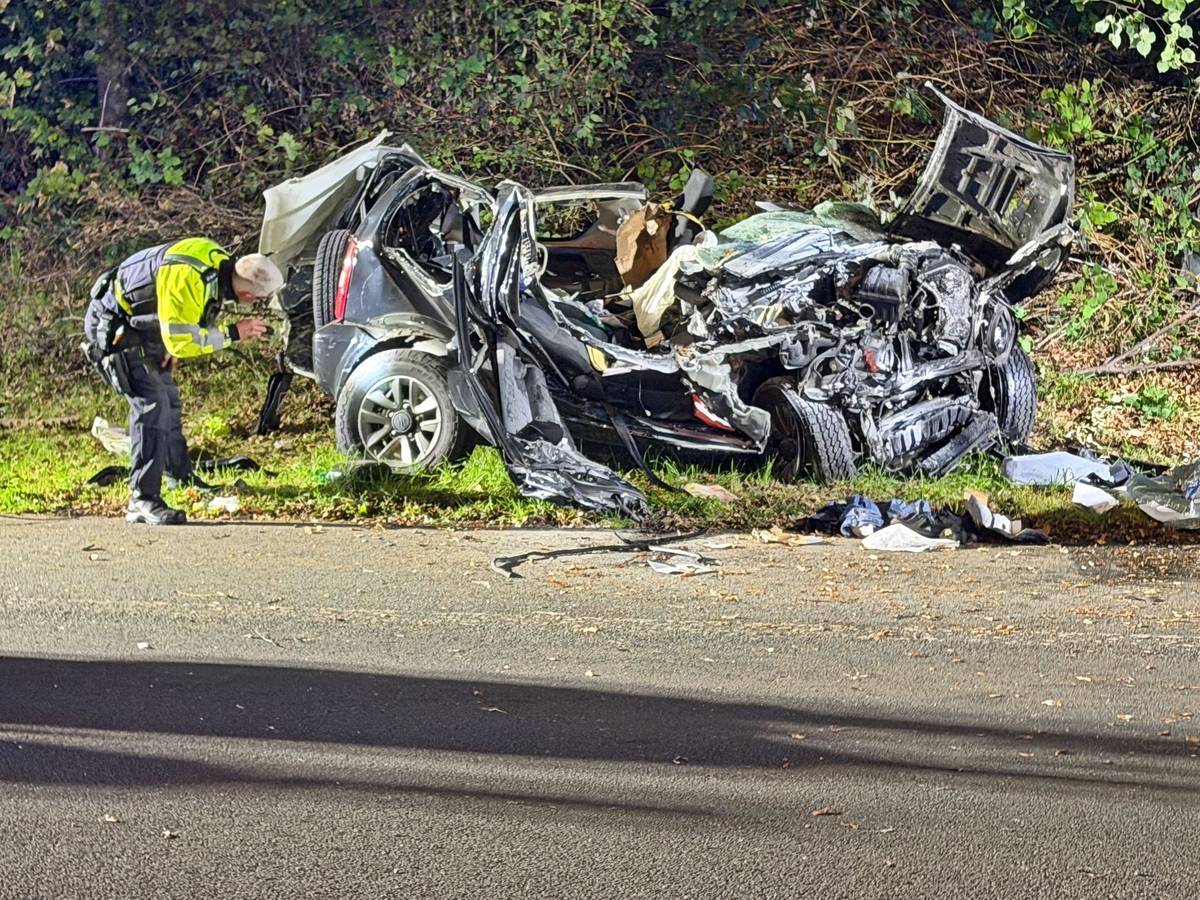 Ein Polizeibeamter untersucht ein zerstörtes Fahrzeug nach einem tödlichen Unfall an einer Autobahnausfahrt in Wuppertal.