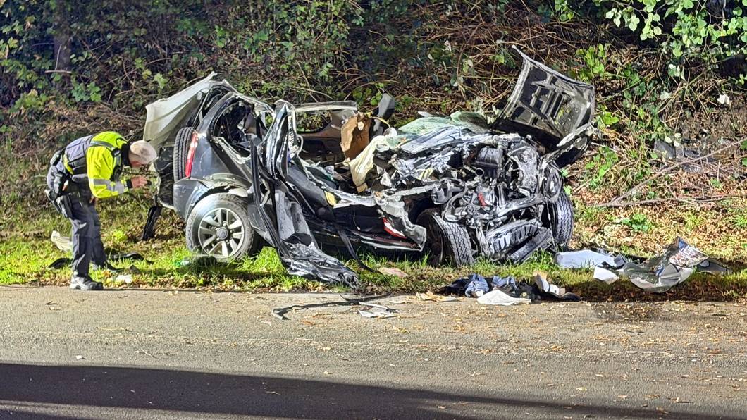 Ein Polizeibeamter untersucht ein zerstörtes Fahrzeug nach einem tödlichen Unfall an einer Autobahnausfahrt in Wuppertal.