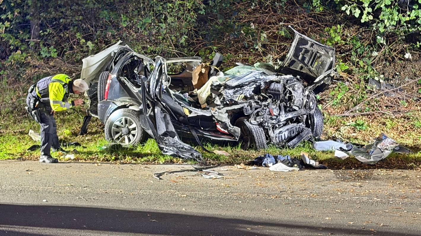 Ein Polizeibeamter untersucht ein zerstörtes Fahrzeug nach einem tödlichen Unfall an einer Autobahnausfahrt in Wuppertal.