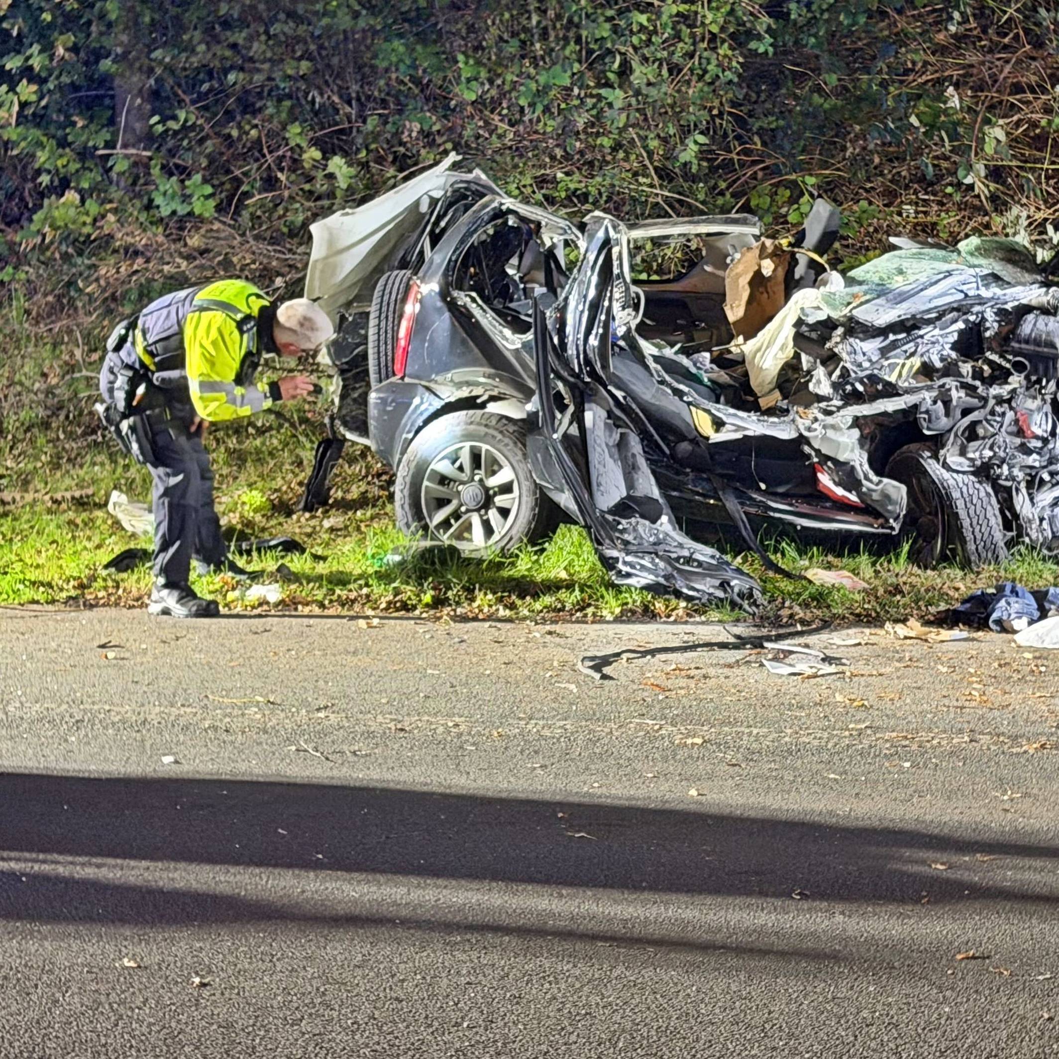 Ein Polizeibeamter untersucht ein zerstörtes Fahrzeug nach einem tödlichen Unfall an einer Autobahnausfahrt in Wuppertal.