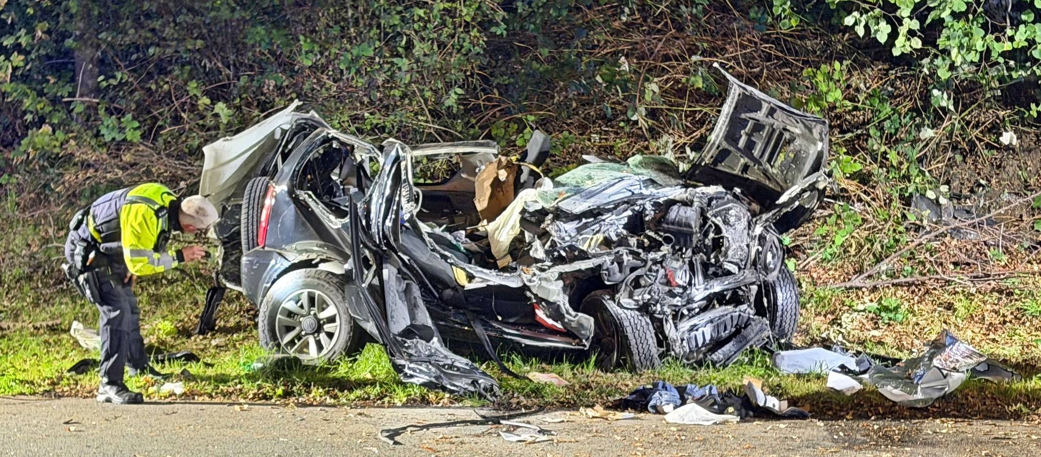 Ein Polizeibeamter untersucht ein zerstörtes Fahrzeug nach einem tödlichen Unfall an einer Autobahnausfahrt in Wuppertal.