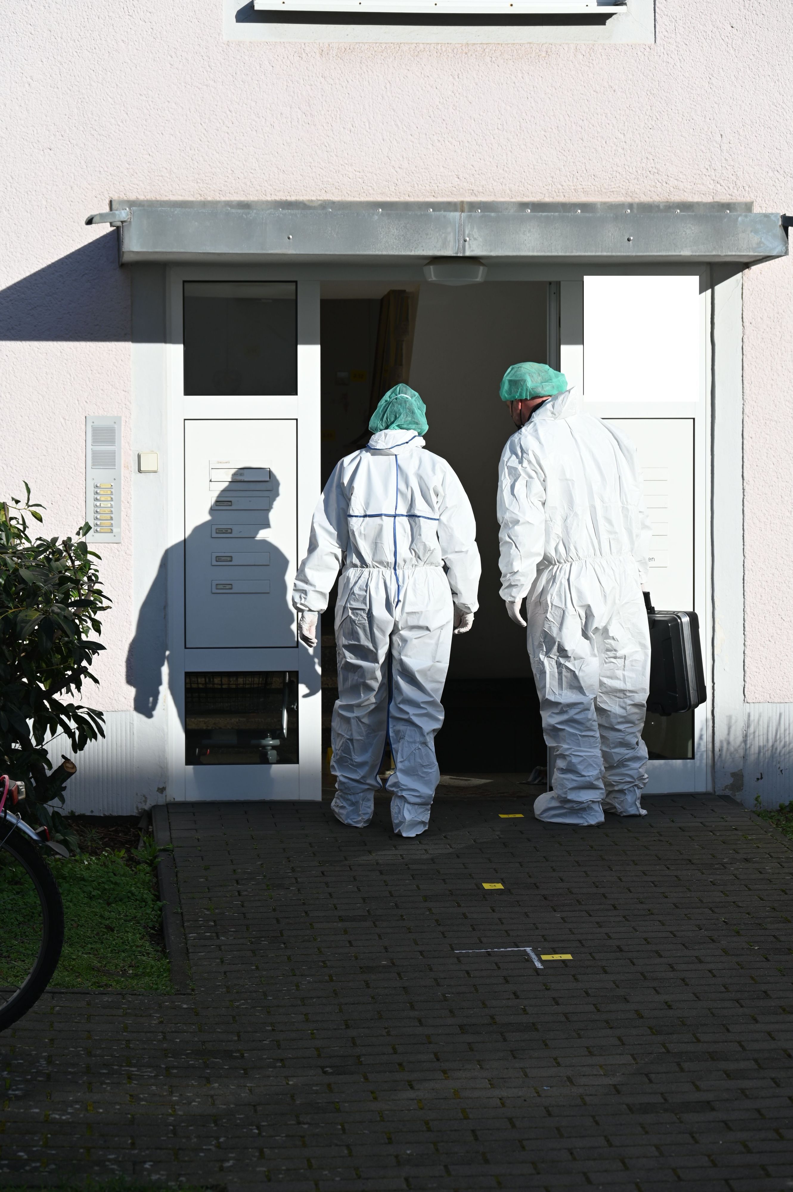 Zwei Kräfte der Spurensicherung betreten in Schutzanzügen ein Haus.