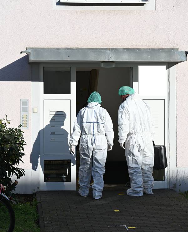 Zwei Kräfte der Spurensicherung betreten in Schutzanzügen ein Haus.