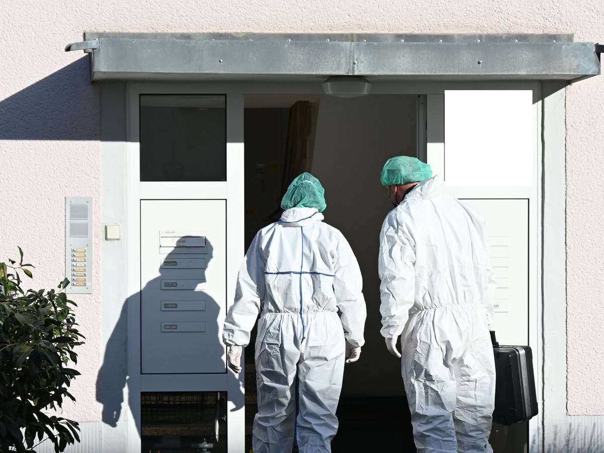 Zwei Kräfte der Spurensicherung betreten in Schutzanzügen ein Haus.