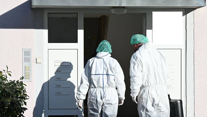 Zwei Kräfte der Spurensicherung betreten in Schutzanzügen ein Haus.