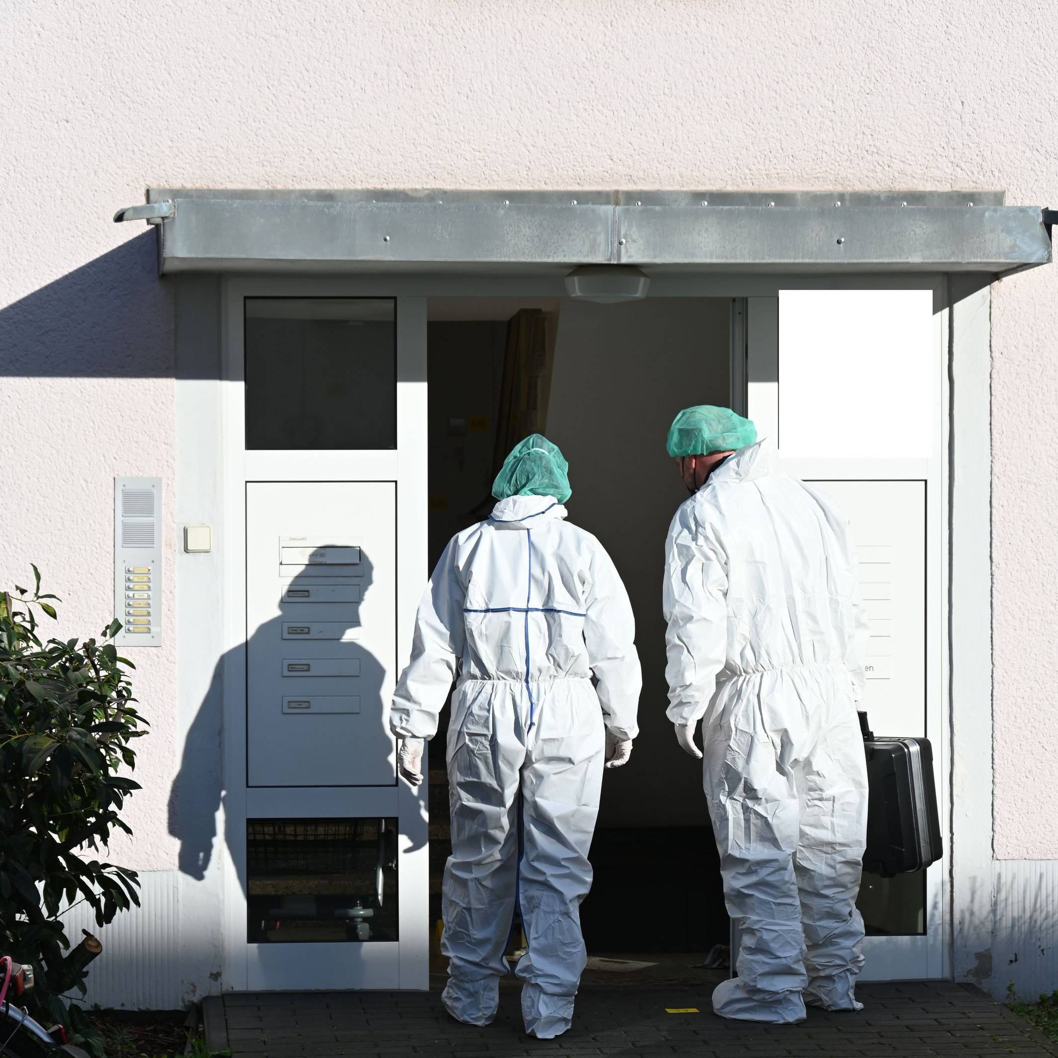 Zwei Kräfte der Spurensicherung betreten in Schutzanzügen ein Haus.