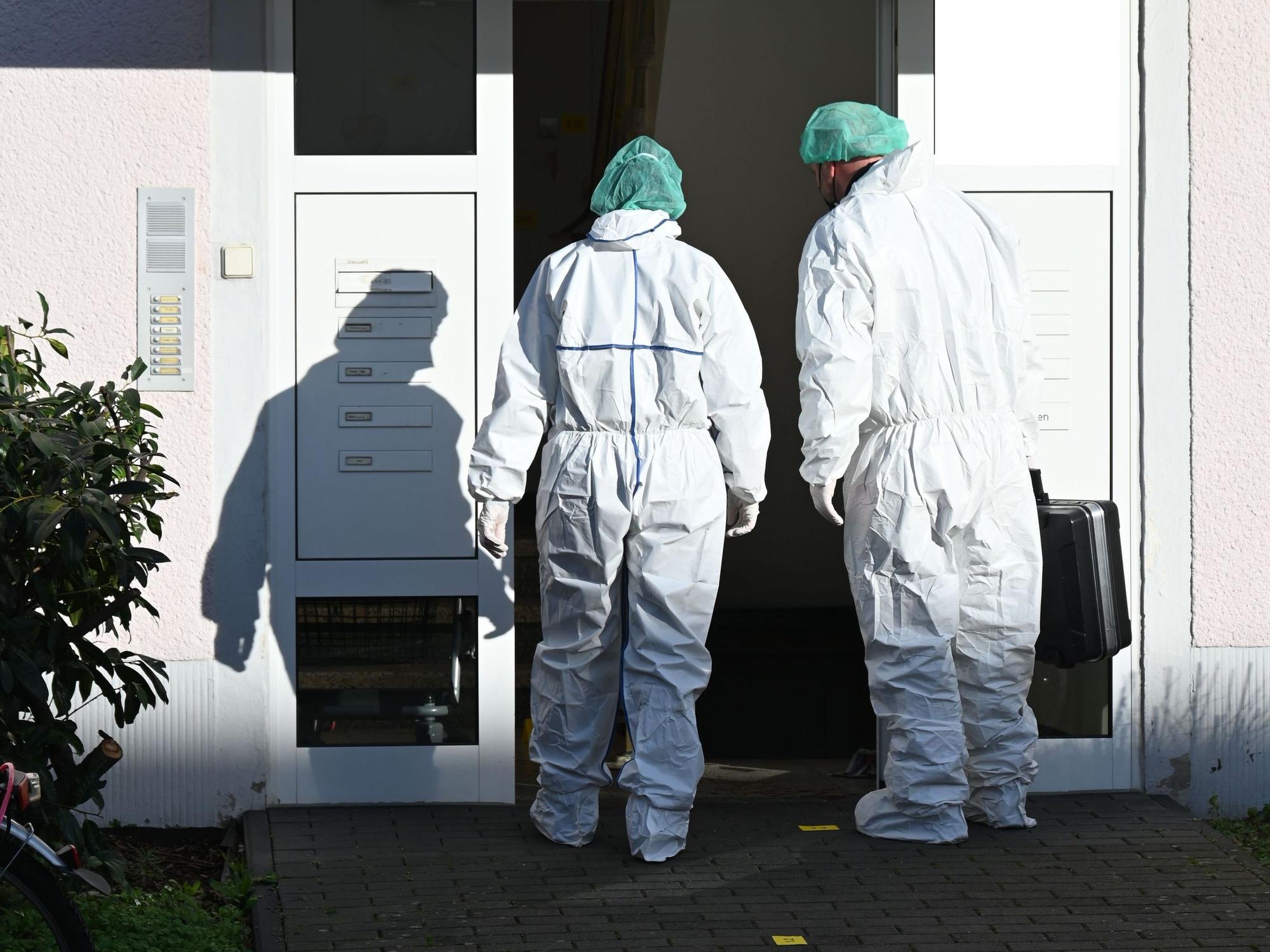 Zwei Kräfte der Spurensicherung betreten in Schutzanzügen ein Haus.