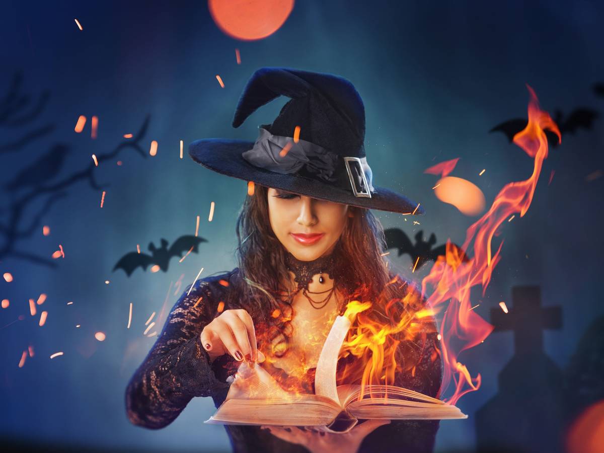 Eine als Hexe verkleidete Frau vor einem brennenden Buch