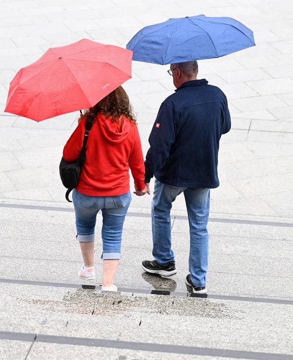 Spaziergänger schützen sich auf dem Bahnhofsvorplatz mit Schirmen vor dem Regen.